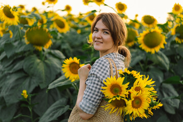 Beautiful young woman with sunflowers enjoying nature and laughing on summer sunflower field. Woman holding sunflowers. Sunflare, sunbeams, glow sun, freedom and happiness concept.