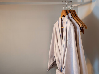 Couple of Japanese style cotton bathrobes hanging on the wooden hangers on the rack inside the white wardrobe for the hotel guest in the dim lights with copy space.