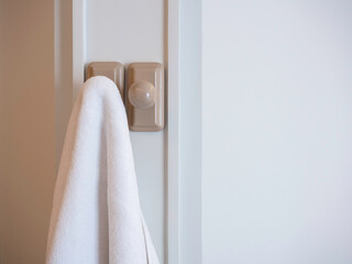 Obraz na płótnie Canvas Close-up white clean towel hanging on a hook, hanger on white wall background in a hotel room with copy space, minimal style.