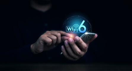 Wi-Fi 6 logo virtual appeared on mobile smartphone while business man's hand using it on dark...
