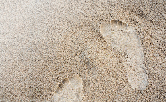 Closeup footprint in the sand beach background. Human foot step track on the wet sand texture with copy space, top view. Vacation, holiday, and summer concept.