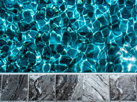 Grey tiles with marble pattern, empty space on the poolside edge floor for objects or summer products placed near the blue water surface of the swimming pool. Mosaic deck pedestal.