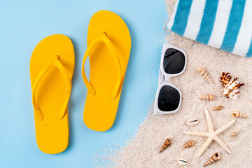 Top view with copy space of yellow sandals with starfish and shells, sand on blue background.