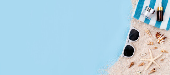 Top view with copy space of cream bottle on sand with starfish and sunglasses on blue background. - Powered by Adobe