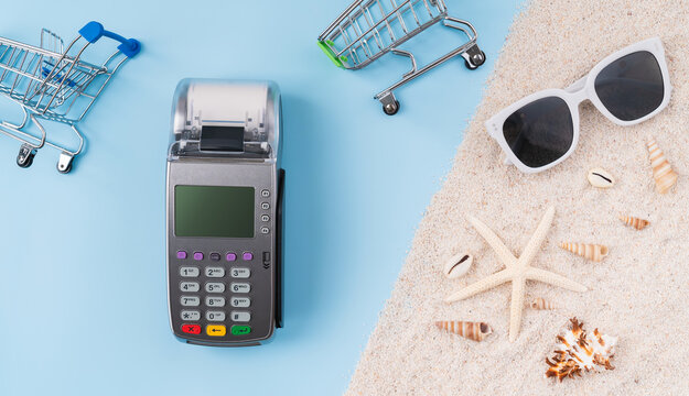 Top view of credit cards and card reader machine with invoice bill and starfish, sunglasses on sand.