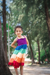 Fototapeta premium Pretty little girl wearing colourful dress and standing near the beach trees.