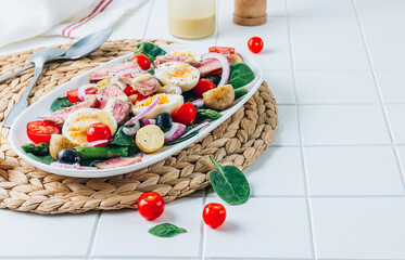 Healthy hearty salad of tuna steak, asparagus, tomatoes, eggs, potatoes and black olives on a white background.
