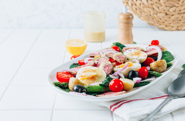 Healthy hearty salad of tuna steak, asparagus, tomatoes, eggs, potatoes and black olives on a white background.