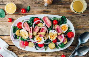 French Salad Nicoise with tuna steak, asparagus, tomatoes, eggs, potatoes and black olives on a white background.