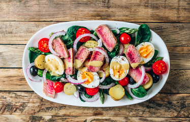 French Salad Nicoise with tuna steak, asparagus, tomatoes, eggs, potatoes and black olives on a white background.