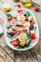French Salad Nicoise with tuna steak, asparagus, tomatoes, eggs, potatoes and black olives on a white background.
