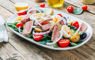 French Salad Nicoise with tuna steak, asparagus, tomatoes, eggs, potatoes and black olives on a white background.