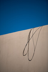 shadow cast onto textured exterior cement concrete or plaster adobe house wall by electric cable with blue sky in background curved lines circular shapes cast onto home wall by afternoon sun vertical 