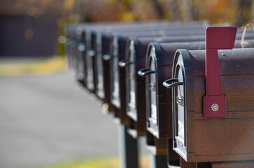 mailboxes in a row line up of multiple U.S. postal service black metal mail boxes in a row first mail box with red flag up signifying mail horizontal format fall background empty space for type  - Powered by Adobe