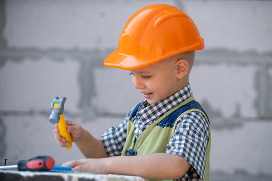 Kid in hard hat holding hammer. Little child helping with toy tools on construciton site. Kids with construction tools. Construction worker. Repair home.