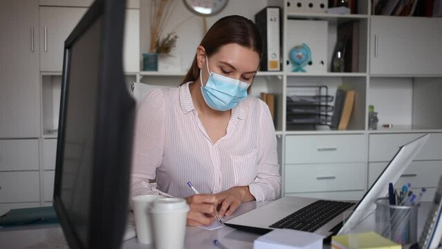 Portrait of young business woman in medical face mask in office. Concept of precautions and social distancing in COVID 19 pandemic. High quality FullHD footage