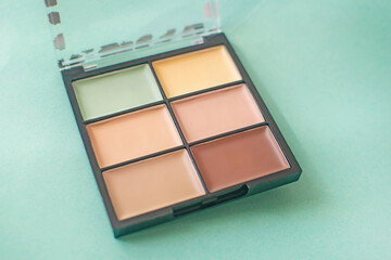 Make-up palette with colorful concealers on mint background.
