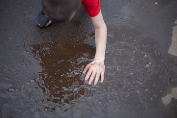 Hand in puddle. Child gets his hand dirty. Boy touches water. Kids love dirt.