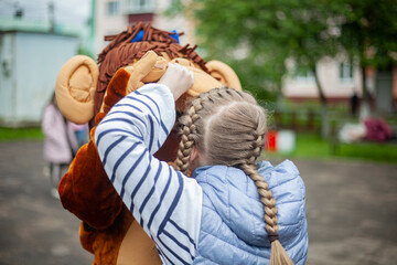 Child plays with growth doll. Animator at festival entertains children. Girl holds man in monkey costume. Rest in park.