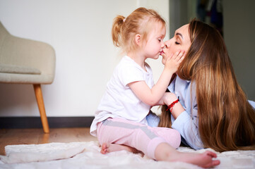 Happy family. Young mom kissing her cute little daughter at home lying on the floor