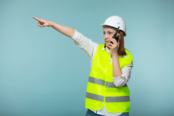 Professional engineer. A woman in a protective helmet and a bright vest gives instructions on a walkie-talkie, on a blue background. Copy paste.