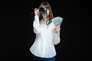 Portrait of a young woman wearing a white shirt holding a camera and US dollars in her hand. The...