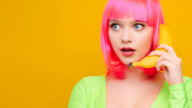 Sexy female woman on pink wig call by banana on bright yellow background