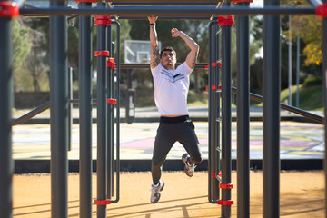 Sportsman working out on sunny day. Man in sportive clothes on open air sports ground, climbing equipment. Sport, health, working out concept - Powered by Adobe
