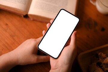 Female using a smartphone over wooden table workspace.