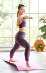 Fototapeta premium Asian young healthy slim beautiful sexy female sporty model in casual crop top sportswear standing stretching arms and legs on yoga mat with exercise ball in pilates gym workout classroom studio