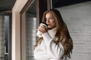 Beautiful woman drinking coffee. Girl holds paper cup of hot coffee.