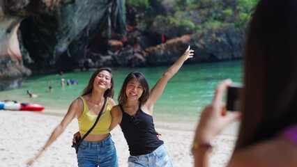 4K Young Asian woman friends using mobile phone photography together while travel in the cave on island beach lagoon in sunny day. Happy female enjoy and fun outdoor lifestyle on summer vacation trip