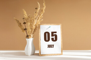 july 5. 5th day of month, calendar date.White vase with dried flowers on desktop in rays of...