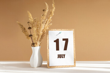 july 17. 17th day of month, calendar date.White vase with dried flowers on desktop in rays of sunlight on white-beige background. Concept of day of year, time planner, summer month