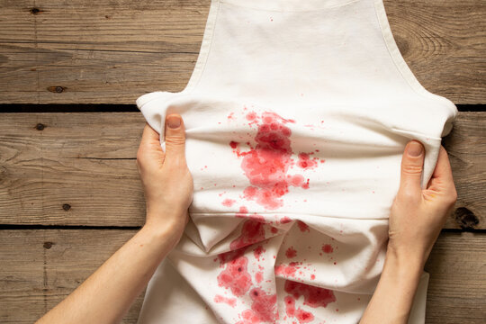 The girl holds in her hands a white dress with red spots, washing dirty clothes