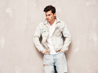 Obraz premium Portrait of handsome confident stylish hipster lambersexual model.Man dressed in jacket and jeans. Fashion male posing in studio near grey wall