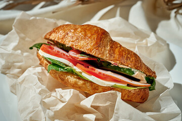 A croissant sandwich with ham, spinach and tomato. Hard Light. White tablecloth.