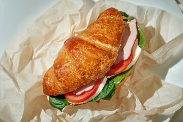 A croissant sandwich with ham, spinach and tomato. Hard Light. White tablecloth.