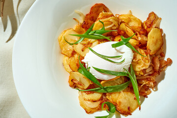 Fried potatoes with a poached egg in a plate. Tough light. White tablecloth.