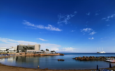Naklejka premium Panorama of a sandy beach in a bay, in the Mediterranean Sea, the largest sailing yacht in the world, an eight-deck motosailer against a blue sky with clouds.