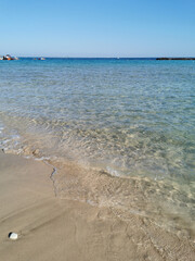 A small wave crashes onto the sandy beach in Fig Tree Bay against a cloudless blue sky.