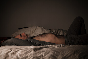 Adult man in open shirt and jeans lying on bed