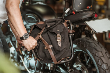 Fototapeta na wymiar rider install a motorcycle saddlebag or side bag on luggage bracket vintage motorbike. motorcycle travel concept. selective focus
