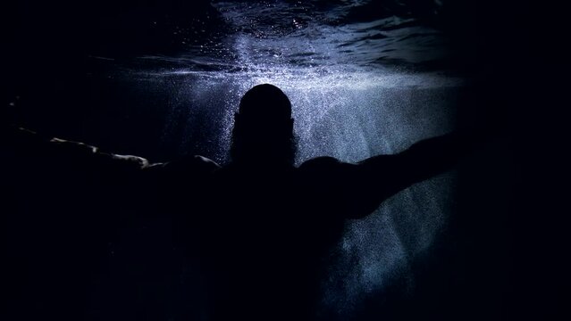 silhouette of a huge bald man in dark water. he poses and raises hands. the middle plan