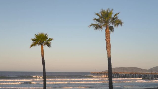Waves rolling on to Pismo Beach with a view of the famous pier and palm trees - slow motion scenic view