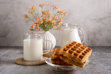 Sweet breakfast of Belgian waffles and a glass of milk on a grey background