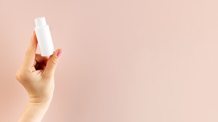 Banner a woman's hand holds a white tube with a cosmetic product on a pink background. Beauty product concept. Sample.