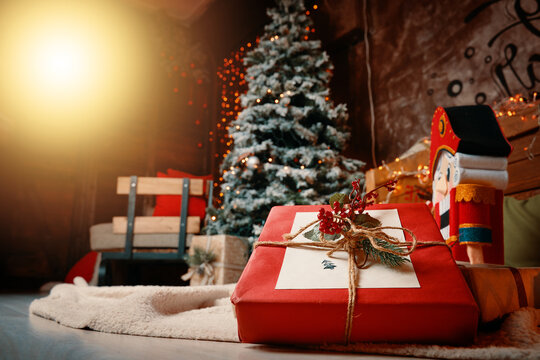 Ornamental gift box and New Year's atmosphere on background. Festive interior in photo studio. Christmas tree, plaid with colorful pillows on floor, Nutcracker figurine and bright garlands on walls.