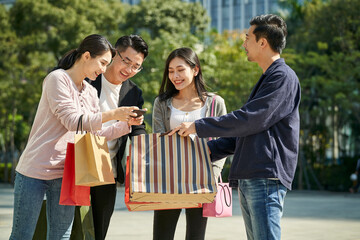 group of young asian people talking looking at cellphone together during shopping trip