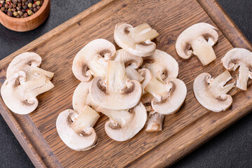 Fototapeta premium Beautiful young white champignons torn to slices on a dark concrete background